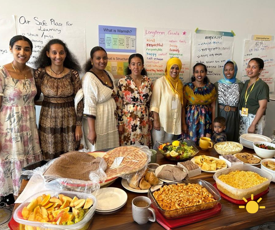 Photograph of Nobody's Perfect participants and facilitators on the final session in June 2024, showcasing a potluck feast of Eritrean food they shared to celebrate.
