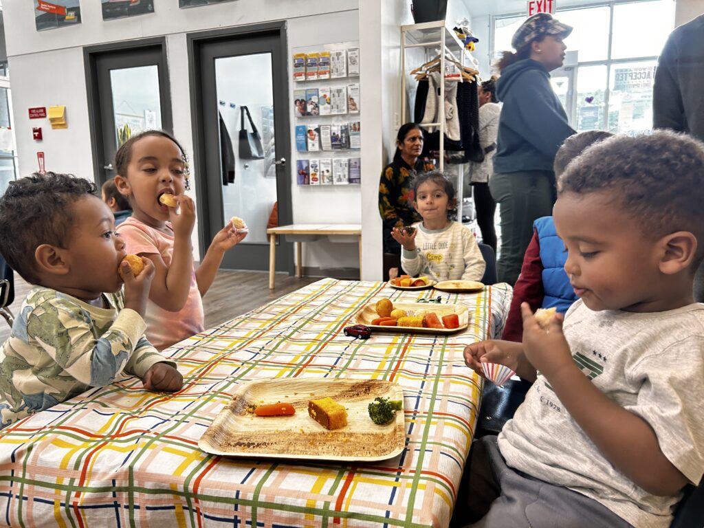 Children sit at the table together and eat food provided at the Eat, Play, Love drop-in at New Westminster Family Place.